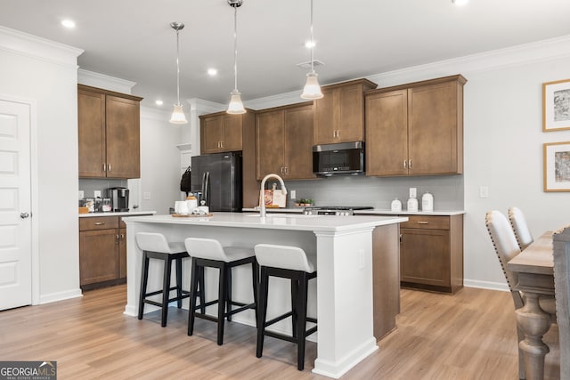 kitchen with a center island with sink, light wood-type flooring, appliances with stainless steel finishes, a kitchen breakfast bar, and pendant lighting