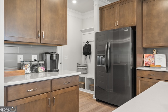 kitchen featuring crown molding, stainless steel fridge, decorative backsplash, and light wood-type flooring