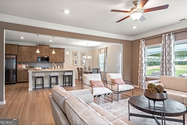 living room featuring ornamental molding, ceiling fan with notable chandelier, and light wood-type flooring