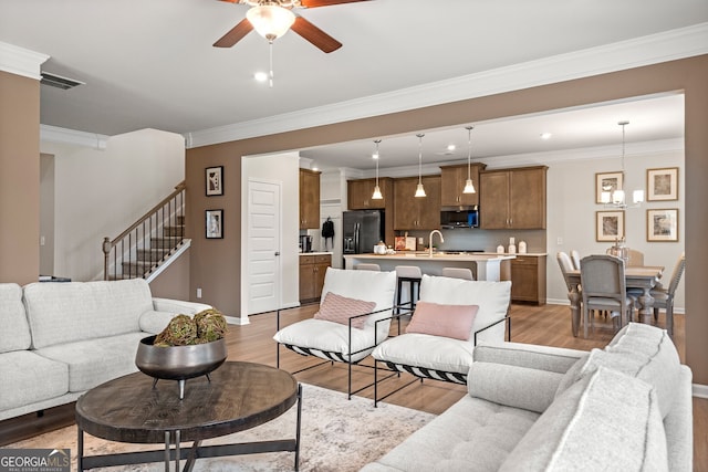 living room with ornamental molding, sink, and light wood-type flooring