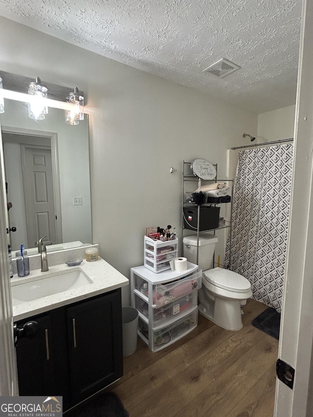 bathroom featuring vanity, wood-type flooring, a textured ceiling, toilet, and walk in shower