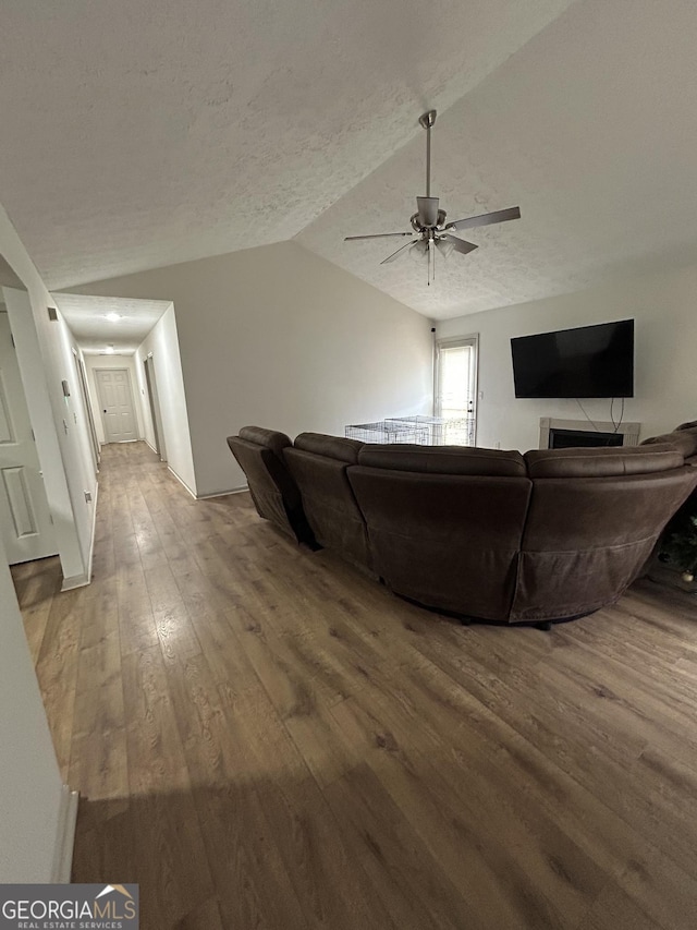 living room featuring wood-type flooring, lofted ceiling, ceiling fan, and a textured ceiling