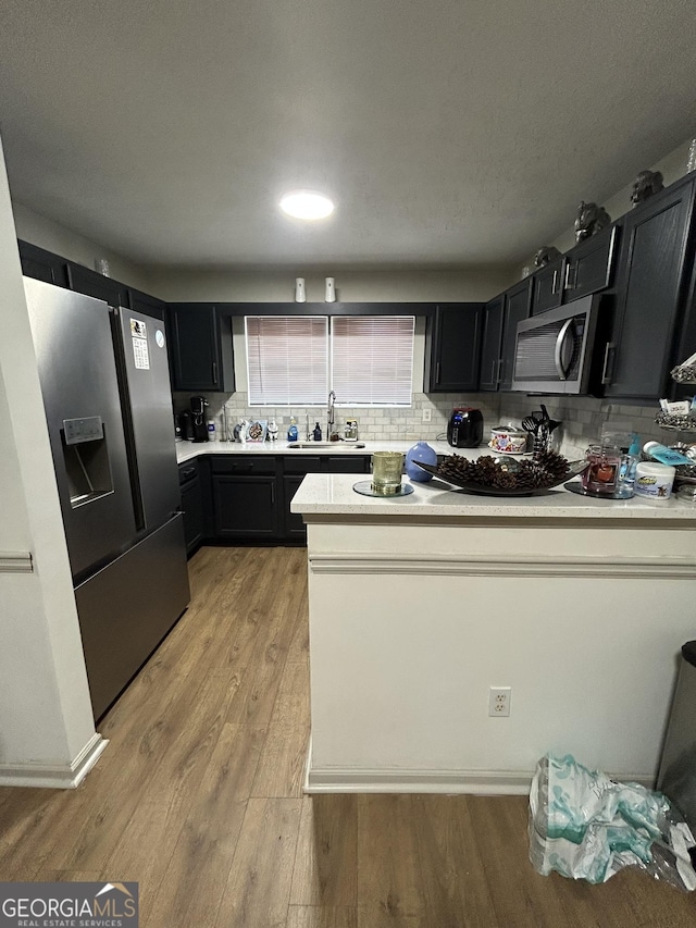 kitchen with tasteful backsplash, sink, stainless steel appliances, and light hardwood / wood-style floors