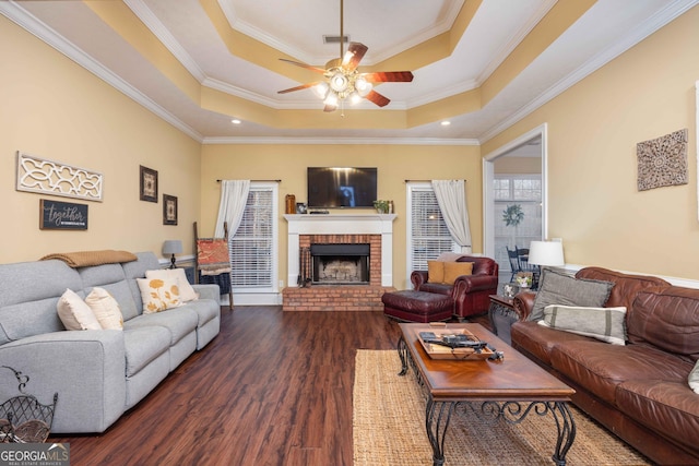 living room with ceiling fan, dark hardwood / wood-style floors, a tray ceiling, a fireplace, and ornamental molding