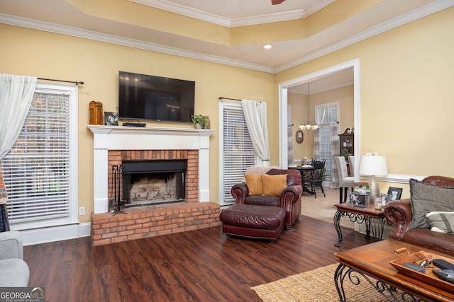 living room with crown molding, a raised ceiling, hardwood / wood-style flooring, ceiling fan, and a fireplace