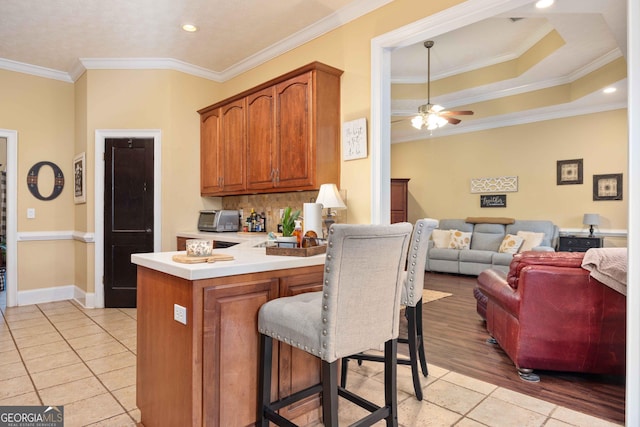 kitchen featuring backsplash, a kitchen breakfast bar, ornamental molding, kitchen peninsula, and a raised ceiling