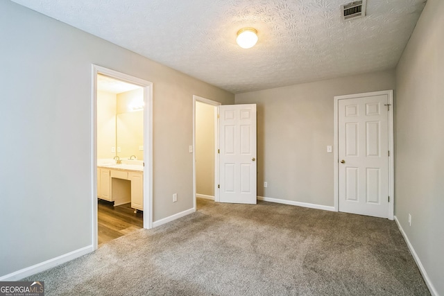 unfurnished bedroom featuring connected bathroom, sink, light colored carpet, and a textured ceiling