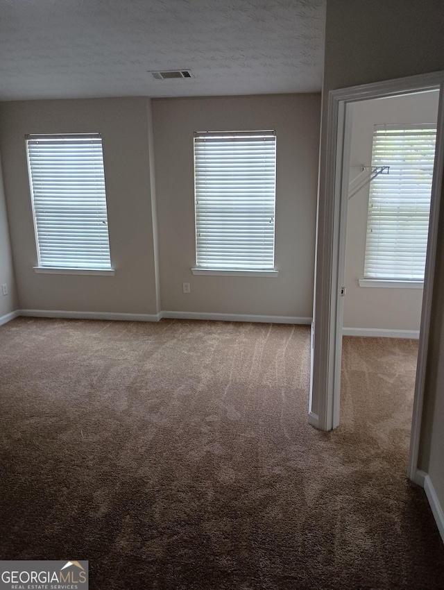 unfurnished room with baseboards, visible vents, a textured ceiling, and carpet flooring