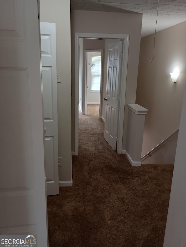 hallway with a barn door, dark carpet, an upstairs landing, and baseboards