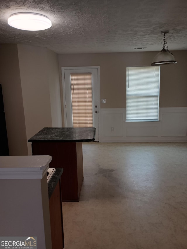 kitchen featuring a wainscoted wall, hanging light fixtures, dark countertops, and a kitchen island