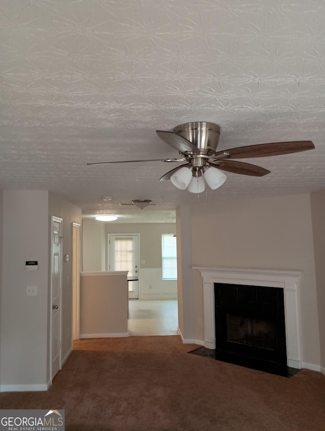 unfurnished living room featuring a fireplace with flush hearth, carpet flooring, ceiling fan, a textured ceiling, and baseboards