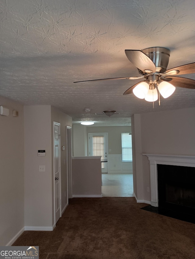 unfurnished living room with a textured ceiling, carpet flooring, a fireplace with flush hearth, a ceiling fan, and baseboards