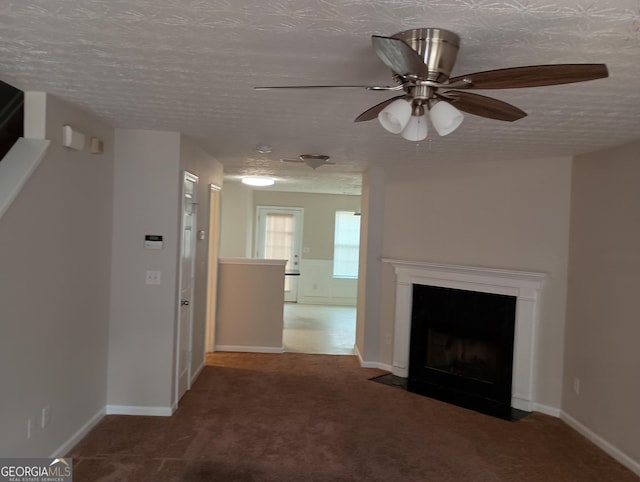 unfurnished living room featuring baseboards, a ceiling fan, a fireplace with flush hearth, a textured ceiling, and dark carpet