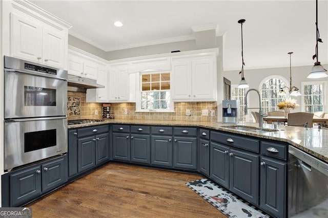 kitchen featuring decorative light fixtures, appliances with stainless steel finishes, stone countertops, white cabinetry, and a sink