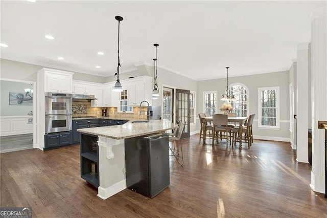 kitchen featuring a kitchen breakfast bar, light stone countertops, white cabinetry, pendant lighting, and a sink