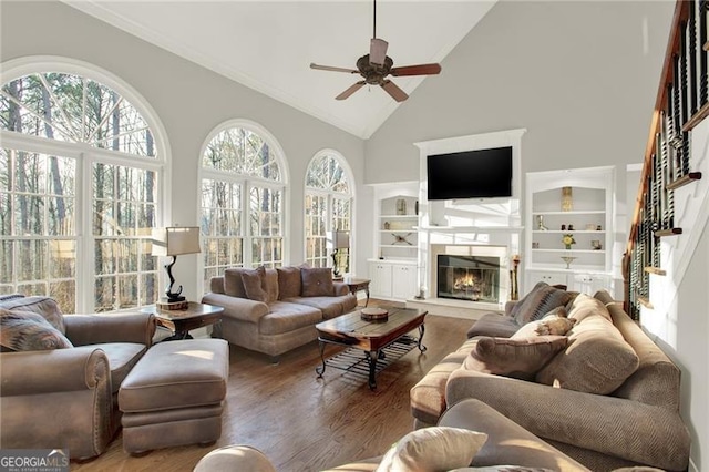 living area with a wealth of natural light, a glass covered fireplace, a ceiling fan, and wood finished floors