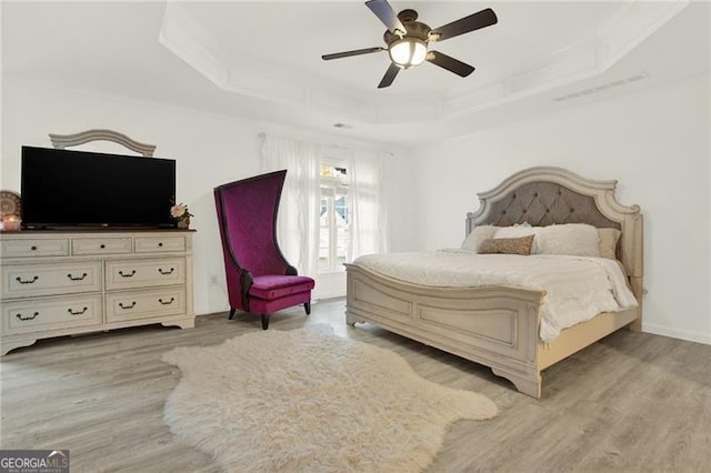 bedroom with a raised ceiling, visible vents, and light wood-style floors