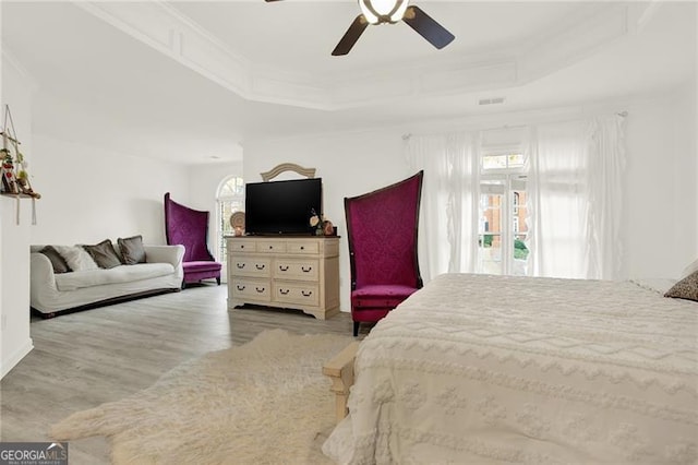 bedroom with multiple windows, light wood-type flooring, a raised ceiling, and visible vents