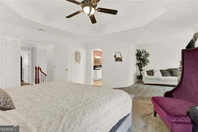 bedroom with light wood finished floors, a raised ceiling, visible vents, ornamental molding, and a ceiling fan