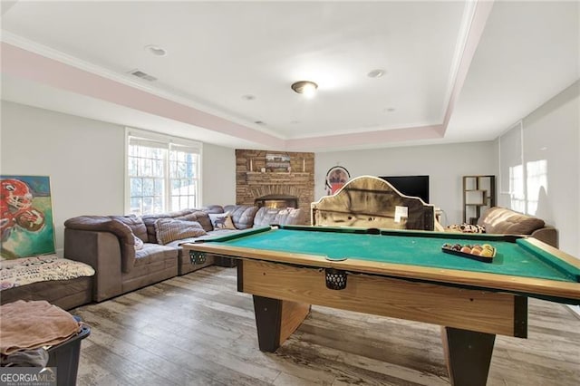 game room featuring a stone fireplace, a tray ceiling, visible vents, and light wood-style floors