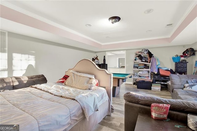 bedroom featuring light wood-style floors, a raised ceiling, visible vents, and ornamental molding