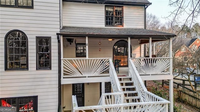 exterior space with a shingled roof, a balcony, stairs, fence, and a porch