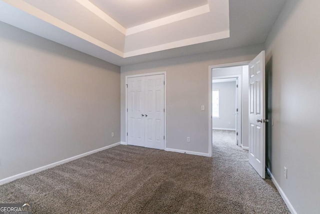 unfurnished bedroom featuring a tray ceiling, a closet, and carpet