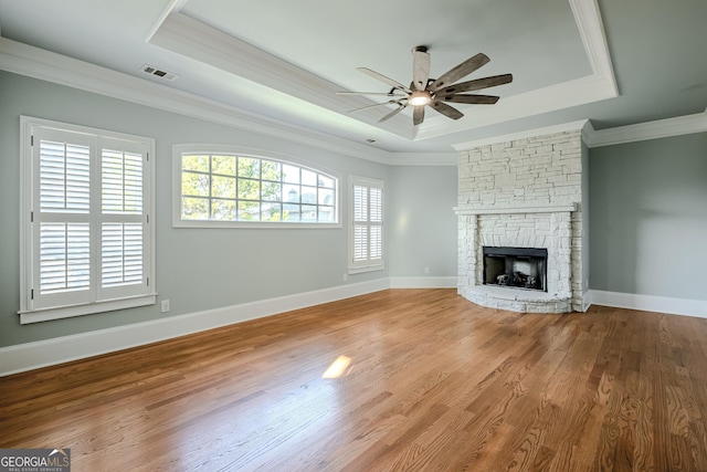 unfurnished living room with crown molding, a tray ceiling, a stone fireplace, and hardwood / wood-style flooring