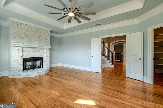 unfurnished living room featuring crown molding, light wood-type flooring, a raised ceiling, ceiling fan, and a fireplace