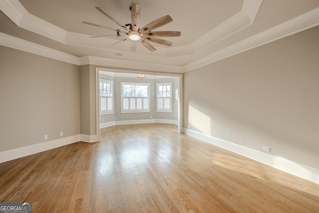 empty room with crown molding, ceiling fan with notable chandelier, light hardwood / wood-style floors, and a raised ceiling