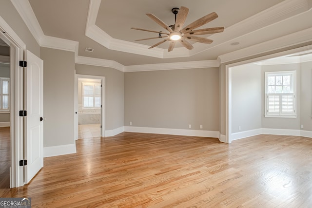 empty room featuring ornamental molding, a raised ceiling, and light wood-type flooring