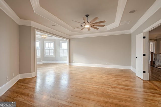 empty room featuring ornamental molding, light wood-type flooring, and a tray ceiling