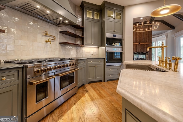 kitchen featuring pendant lighting, sink, stainless steel appliances, custom range hood, and light wood-type flooring