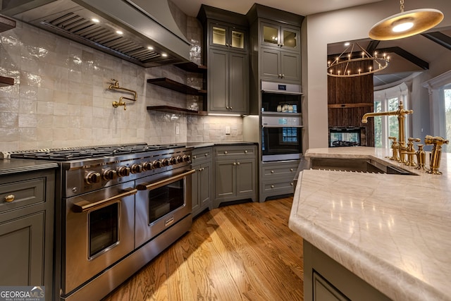 kitchen with sink, light hardwood / wood-style flooring, appliances with stainless steel finishes, hanging light fixtures, and custom exhaust hood