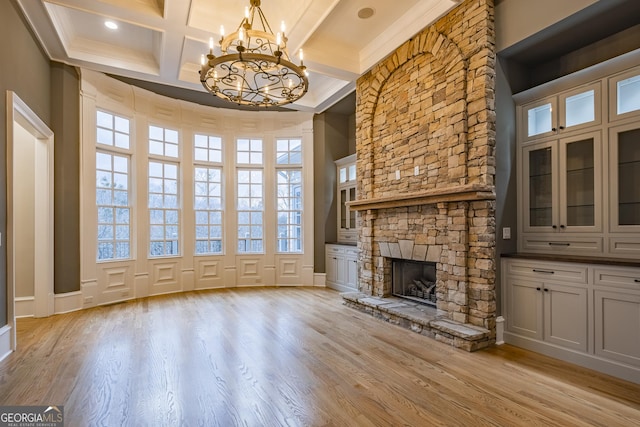 unfurnished living room featuring a stone fireplace, a wealth of natural light, beamed ceiling, coffered ceiling, and light hardwood / wood-style flooring