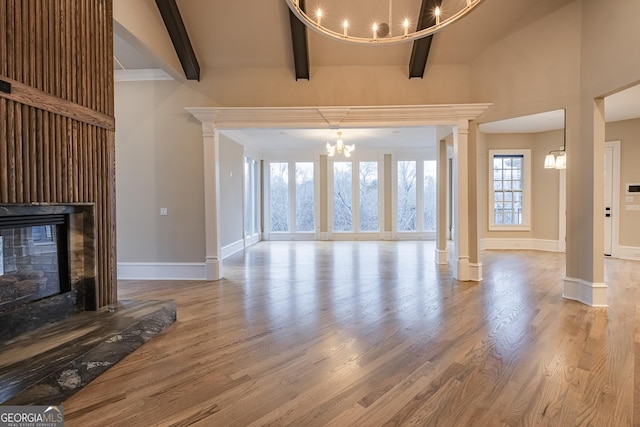 unfurnished living room featuring ornate columns, wood-type flooring, a notable chandelier, and beam ceiling