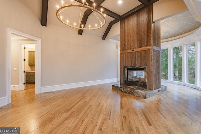 unfurnished living room with a multi sided fireplace, an inviting chandelier, and light hardwood / wood-style floors