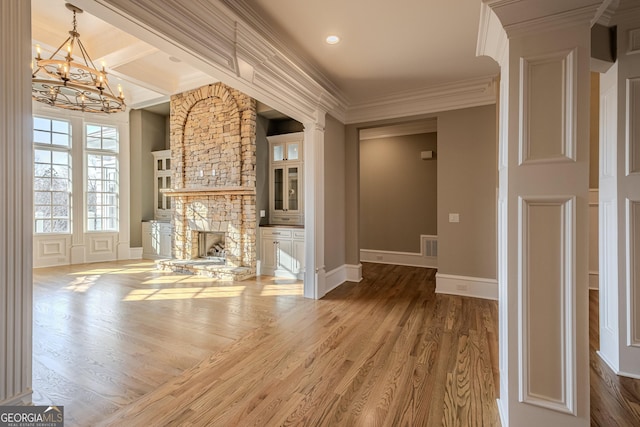 unfurnished living room with a notable chandelier, a stone fireplace, wood-type flooring, and ornamental molding