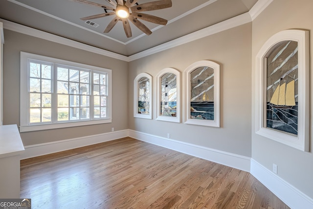 empty room with crown molding, ceiling fan, a tray ceiling, and light wood-type flooring