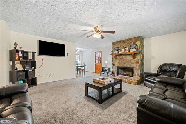 carpeted living room featuring ceiling fan, a stone fireplace, and a textured ceiling