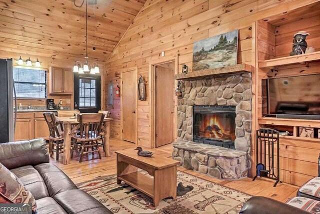 living room with wood ceiling, wood walls, a notable chandelier, a stone fireplace, and light wood-type flooring