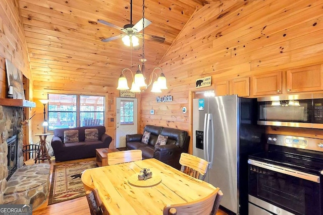 kitchen with appliances with stainless steel finishes, hanging light fixtures, wooden walls, high vaulted ceiling, and a fireplace