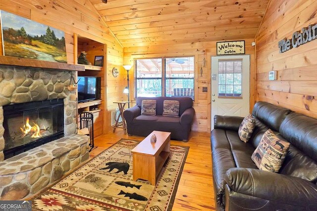 living room featuring light hardwood / wood-style flooring, a stone fireplace, vaulted ceiling, and wooden walls