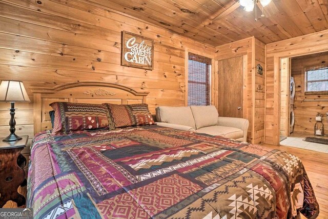 bedroom featuring stacked washer and dryer, wood ceiling, light wood-type flooring, and wood walls