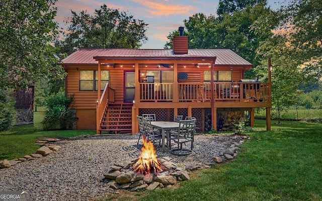 back of house at dusk with a fire pit, stairway, a wooden deck, a lawn, and a chimney