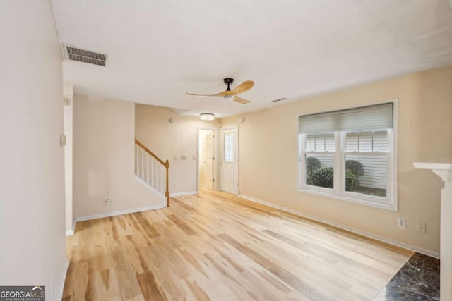 unfurnished living room with a ceiling fan, visible vents, baseboards, stairway, and light wood-type flooring