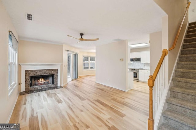 unfurnished living room with ceiling fan, a healthy amount of sunlight, a fireplace, and light hardwood / wood-style flooring