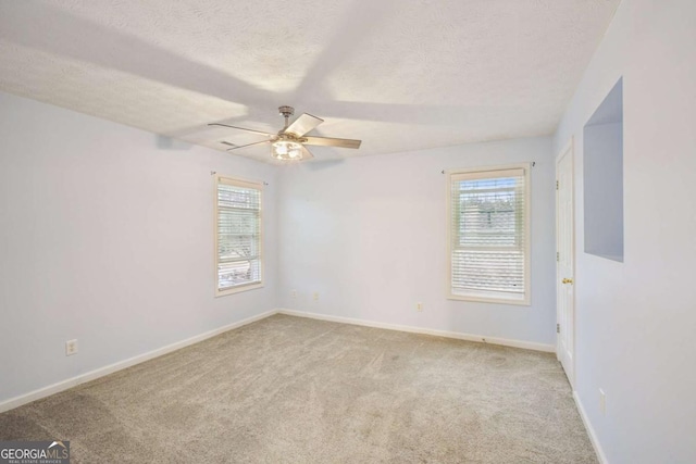 empty room with a textured ceiling, plenty of natural light, baseboards, and light colored carpet