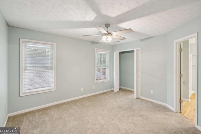 unfurnished bedroom featuring a ceiling fan, light colored carpet, a textured ceiling, and baseboards