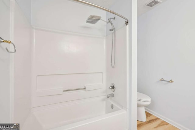 bathroom with hardwood / wood-style flooring, shower / bathing tub combination, and toilet